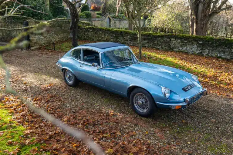 Jaguar E-Type Serie 1 4.2 Fixed Head Coupé 1965 in Opalescent Silver Blue, geparkt im Freien auf einem mit Laub bedeckten Kiesweg.