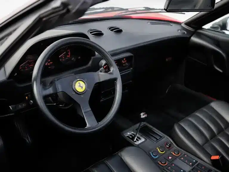 Schwarzer Innenraum mit Lenkrad und Schaltkulisse eines Ferrari 328 GTS von 1988.