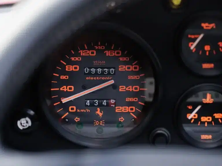 Nahaufnahme des Tachometers eines Ferrari 328 GTS, der eine Laufleistung von 9.830 Kilometern anzeigt.