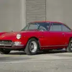 Ferrari 330 GT 2+2 Serie II Baujahr 1966 in Rot, Seitenansicht vor einer grauen Mauer, klassisches Coupé mit stilvollem Design.