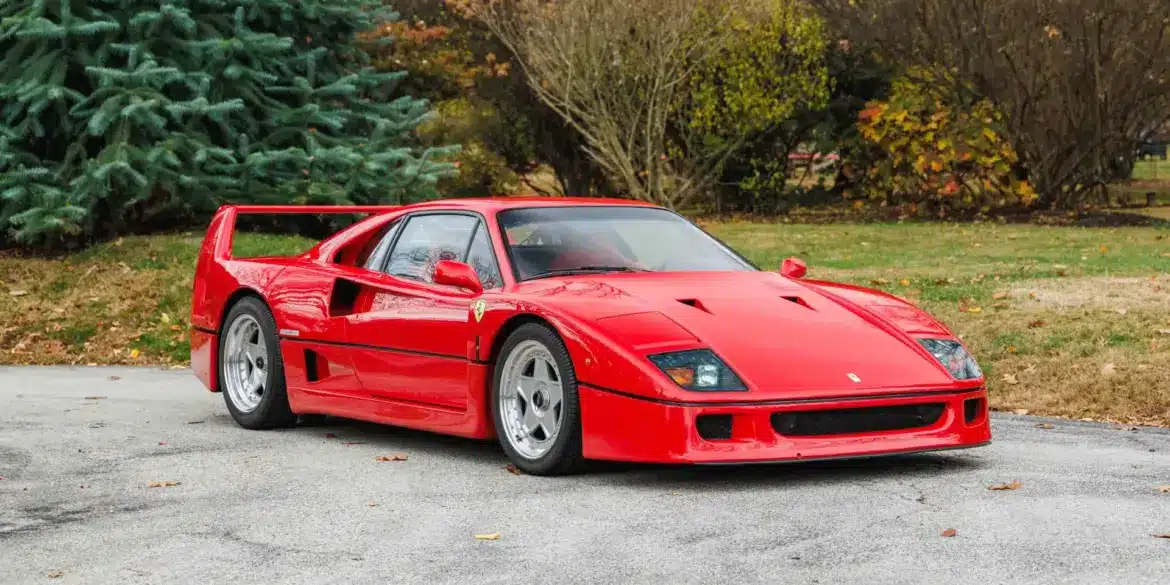 Ferrari F40 in Rot, Baujahr 1991, frontal seitlich fotografiert auf einer Straße vor Bäumen.