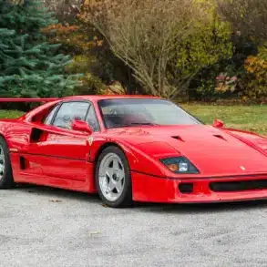 Ferrari F40 in Rot, Baujahr 1991, frontal seitlich fotografiert auf einer Straße vor Bäumen.