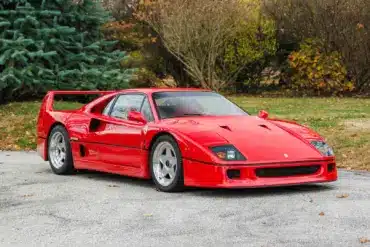 Ferrari F40 in Rot, Baujahr 1991, frontal seitlich fotografiert auf einer Straße vor Bäumen.