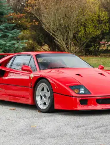 Ferrari F40 in Rot, Baujahr 1991, frontal seitlich fotografiert auf einer Straße vor Bäumen.