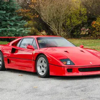 Ferrari F40 in Rot, Baujahr 1991, frontal seitlich fotografiert auf einer Straße vor Bäumen.