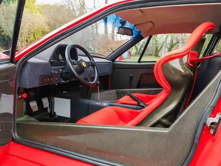 Innenraumaufnahme eines Ferrari F40 mit roten Sportsitzen und sichtbarem Carbon, Minimalismus und Funktionalität stehen im Vordergrund.