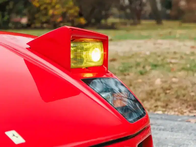 Klappscheinwerfer eines Ferrari F40 in leuchtendem Rot, Nahaufnahme mit eingeschaltetem Licht.