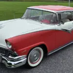 Zweifarbiger Ford Fairlane von 1956, aus schräger Frontperspektive, auf einer Straße stehend, mit auffälligen Heckflossen und Chromdetails.