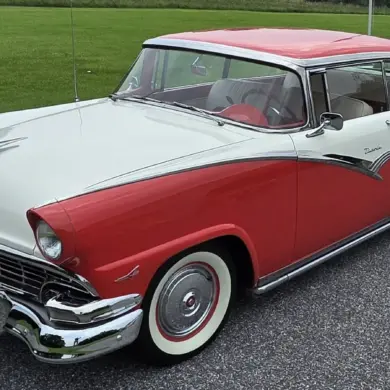 Zweifarbiger Ford Fairlane von 1956, aus schräger Frontperspektive, auf einer Straße stehend, mit auffälligen Heckflossen und Chromdetails.