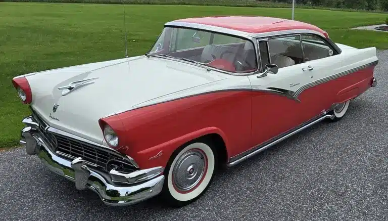 Zweifarbiger Ford Fairlane von 1956, aus schräger Frontperspektive, auf einer Straße stehend, mit auffälligen Heckflossen und Chromdetails.