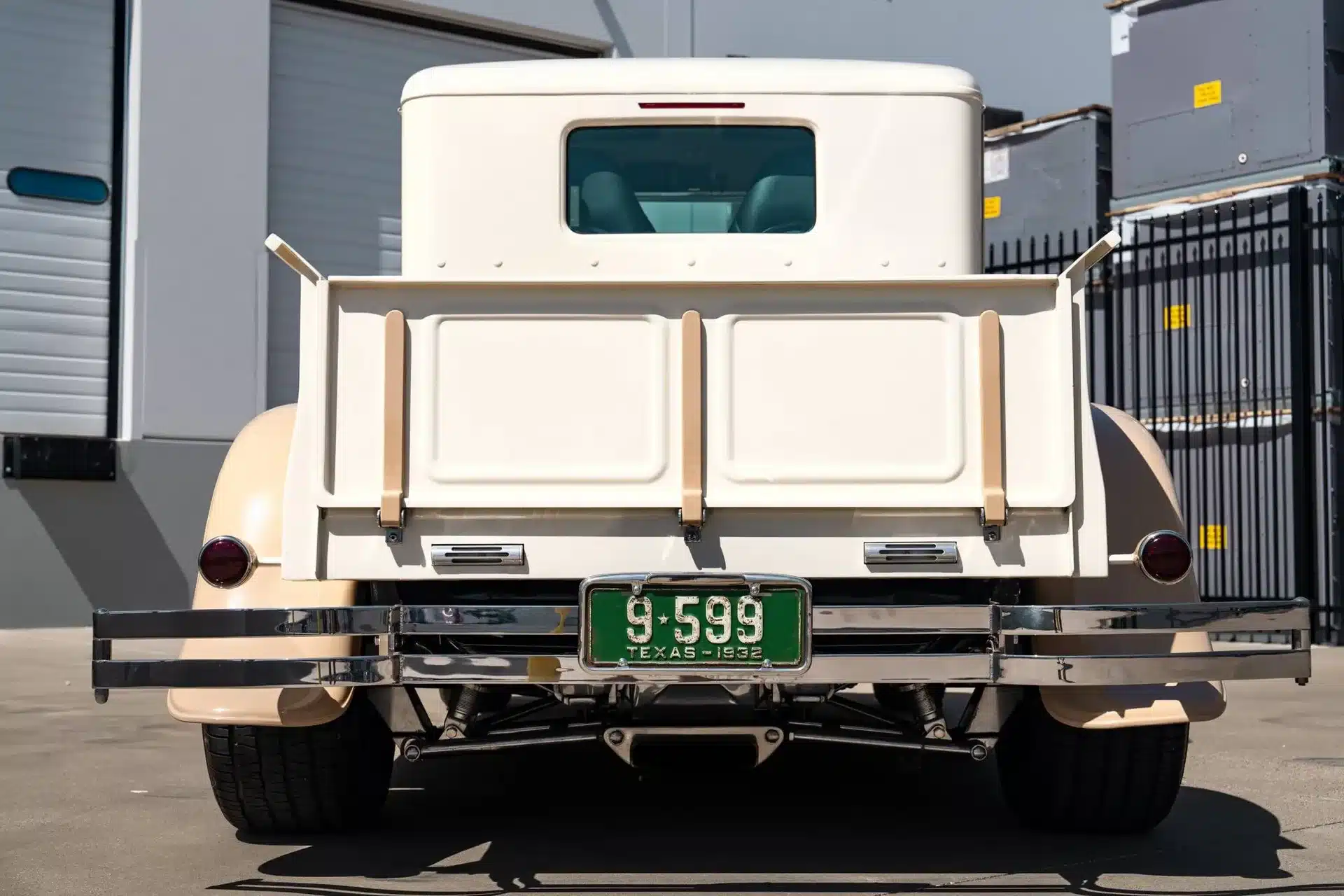 Heckansicht eines cremefarbenen Ford Pickups von 1932 mit texanischem Nummernschild, aufgenommen im Freien vor moderner Industriearchitektur