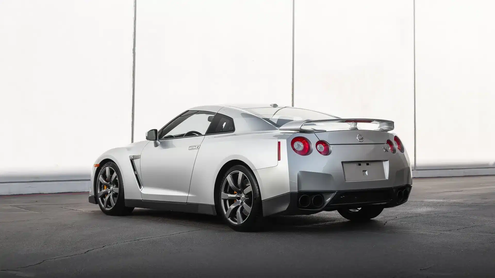 Heckansicht eines silbernen Nissan GT-R R35 Baujahr 2009 auf Asphalt vor hellem Hintergrund.