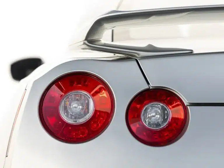 Die charakteristischen runden Rückleuchten und der markante Heckspoiler eines silbernen Nissan GT-R R35, Baujahr 2009, Nahaufnahme.