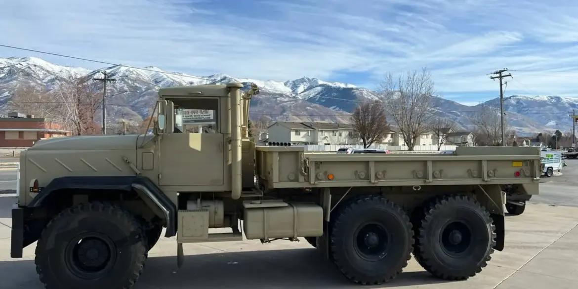 AM General M939 Militär-Lkw Baujahr 1985, beige lackiert, mit drei Achsen und robuster Karosserie vor Bergpanorama