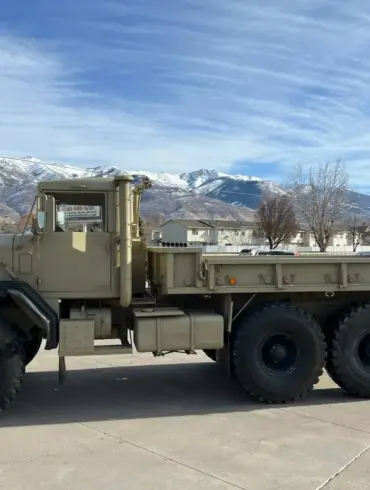AM General M939 Militär-Lkw Baujahr 1985, beige lackiert, mit drei Achsen und robuster Karosserie vor Bergpanorama