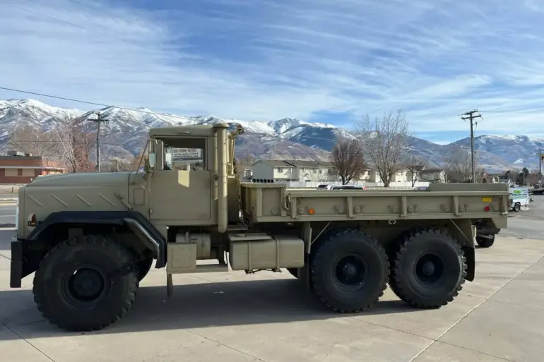 AM General M939 Militär-Lkw Baujahr 1985, beige lackiert, mit drei Achsen und robuster Karosserie vor Bergpanorama