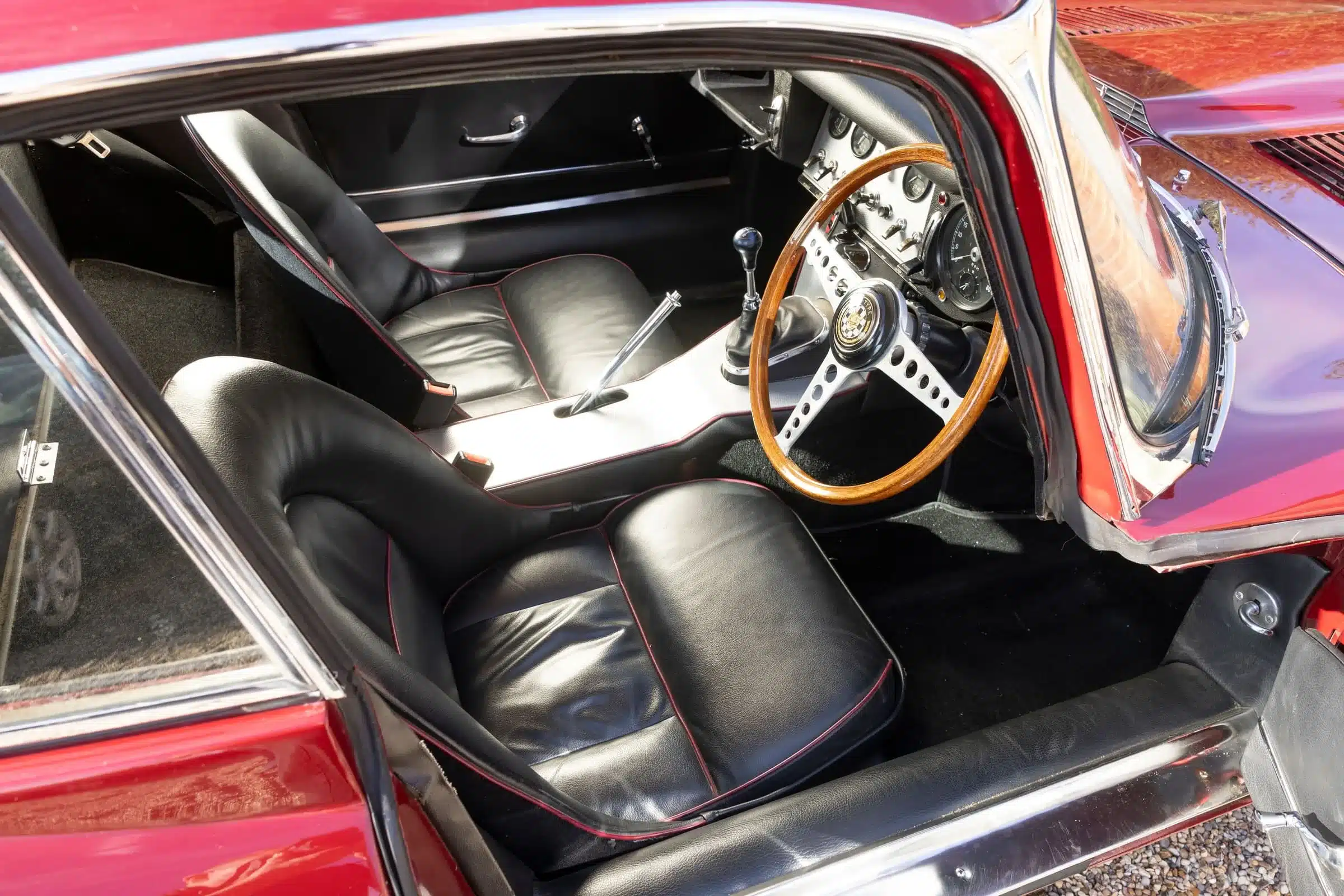 Blick in den Innenraum eines Jaguar E-Type 3.8 Litre Coupé von 1962 mit schwarzem Leder und Holzlenkrad.