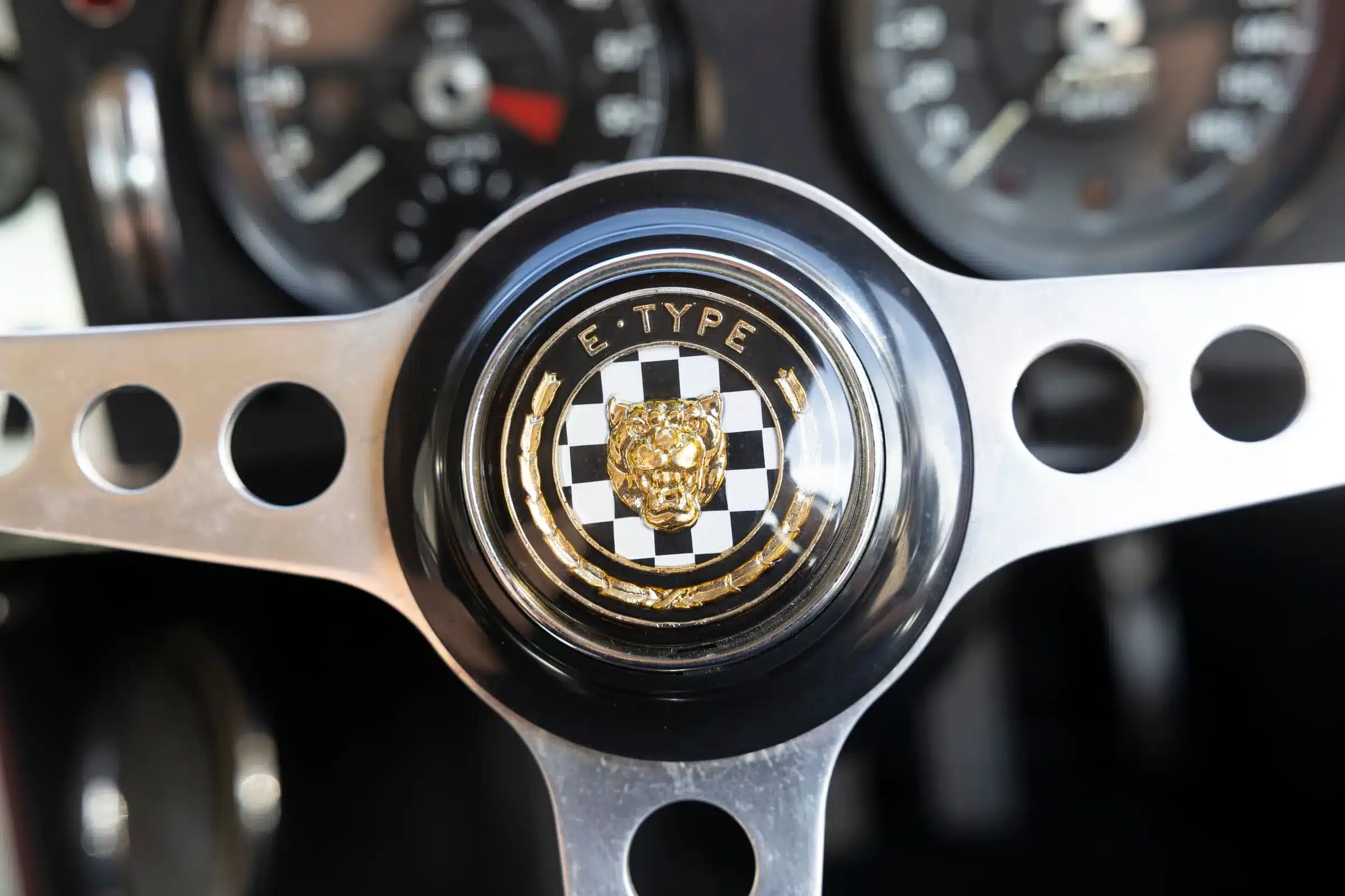 Jaguar E-Type Lenkrad mit goldenem Emblem, im Hintergrund klassische Instrumente