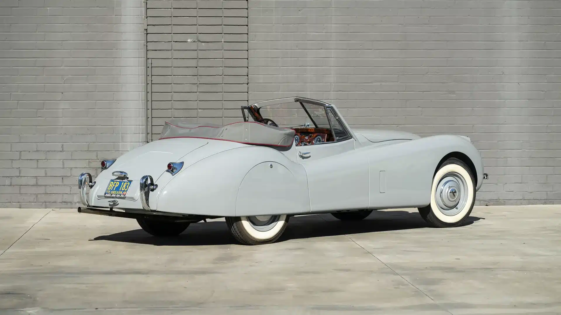 Seltenes Jaguar XK 120 Drophead Coupé von 1953 in Birch Grey mit geschlossenem Verdeck, aufgenommen vor einer grauen Mauer.