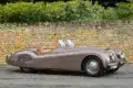 Seitenansicht eines braunen Jaguar XK120 Roadster von 1950 vor einer Steinmauer
