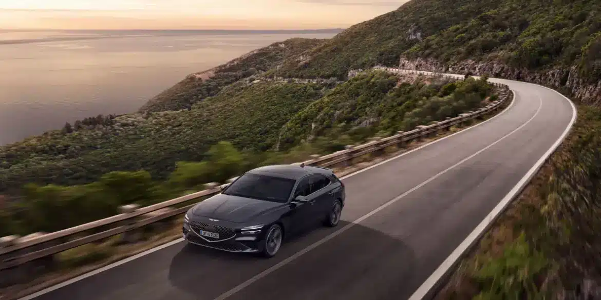 Genesis G70 Shooting Brake in Dunkelgrau auf einer malerischen Küstenstraße mit Panorama-Ausblick bei Sonnenuntergang.