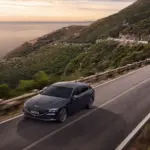 Genesis G70 Shooting Brake in Dunkelgrau auf einer malerischen Küstenstraße mit Panorama-Ausblick bei Sonnenuntergang.