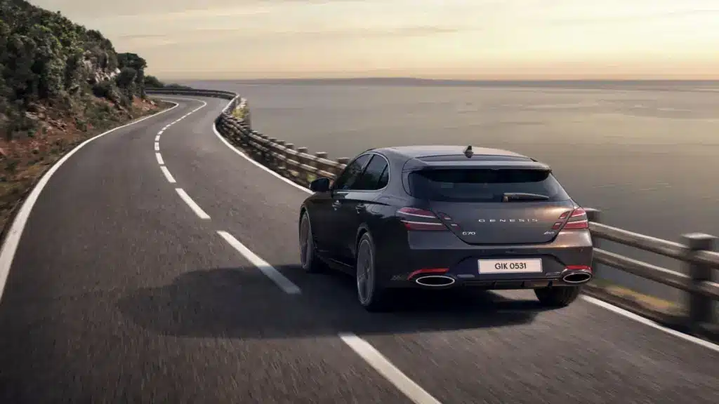 Genesis G70 Shooting Brake auf offener Straße am Meer, Rückansicht bei Sonnenuntergang