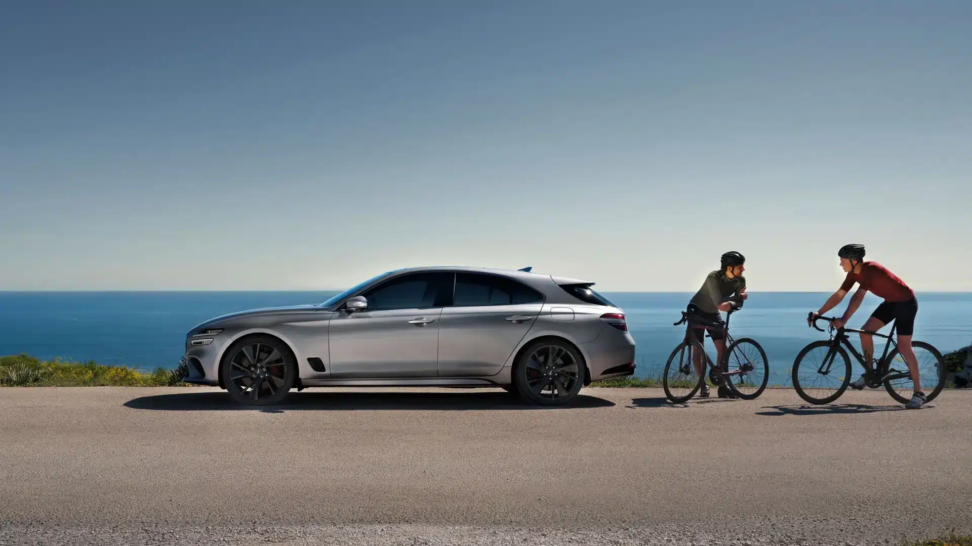 Genesis G70 Shooting Brake in Seitenansicht an der Küste mit zwei Radfahrern im Gespräch.