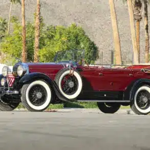 Lincoln Model L Sport Touring by Locke von 1929, kastanienrot mit schwarzen Kotflügeln, offen, mit weißen Wandreifen und zwei seitlichen Ersatzrädern.