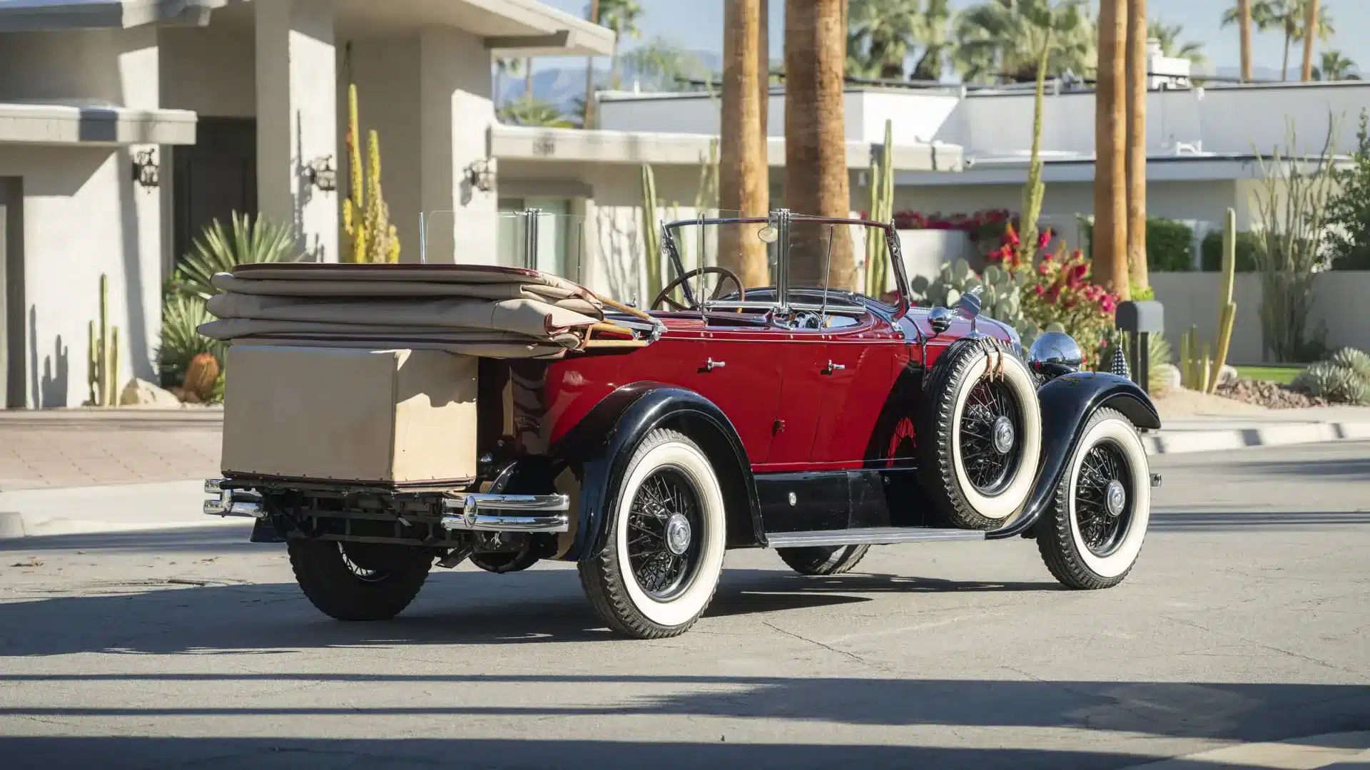 Lincoln Model L Sport Touring by Locke von 1929 mit offenem Verdeck und zwei seitlich montierten Ersatzrädern, abgebildet auf einer Straße vor moderner Bebauung und Palmen.