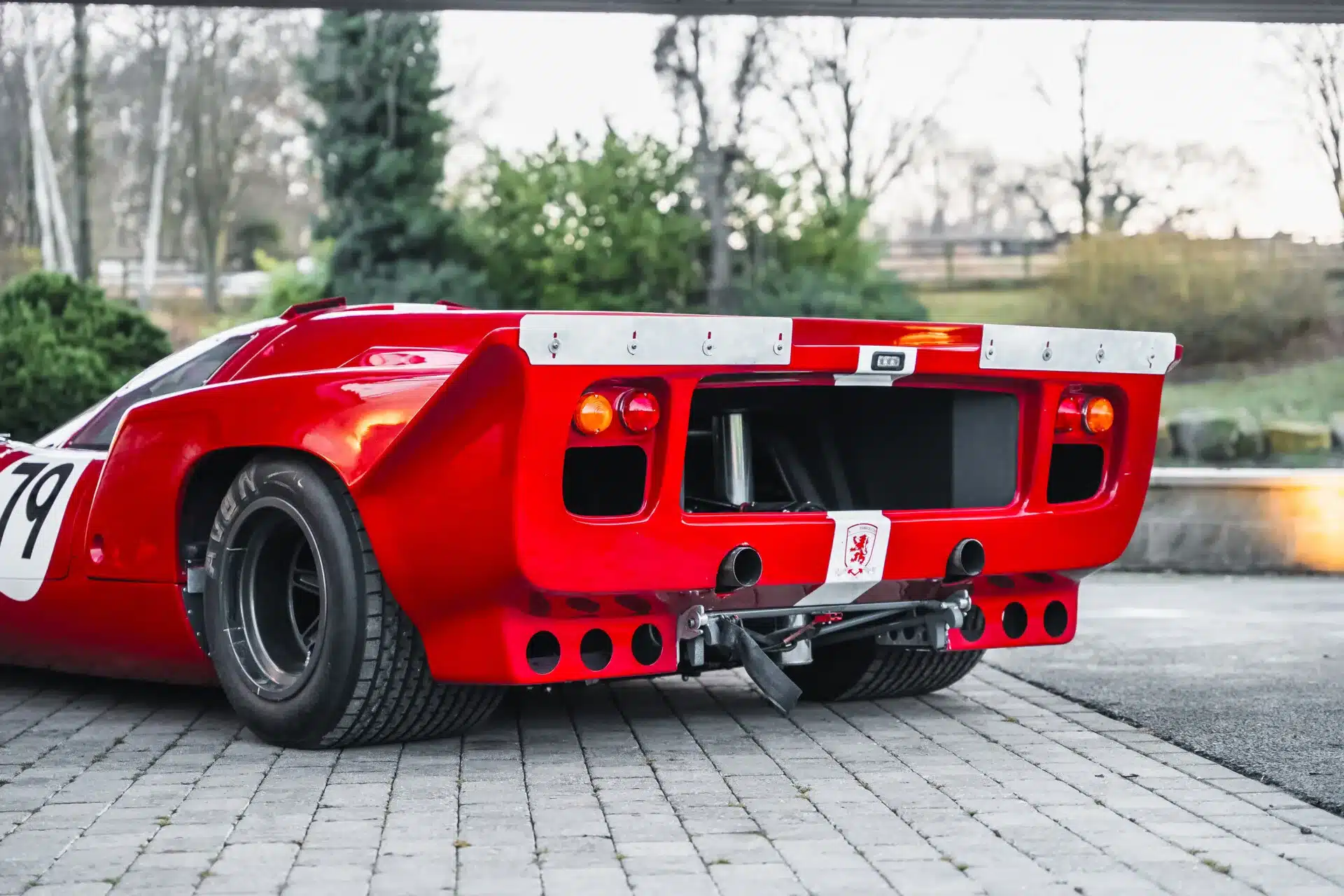Heckansicht eines roten Lola T70 Mk3B Rennwagens auf gepflastertem Untergrund mit Startnummer 79.