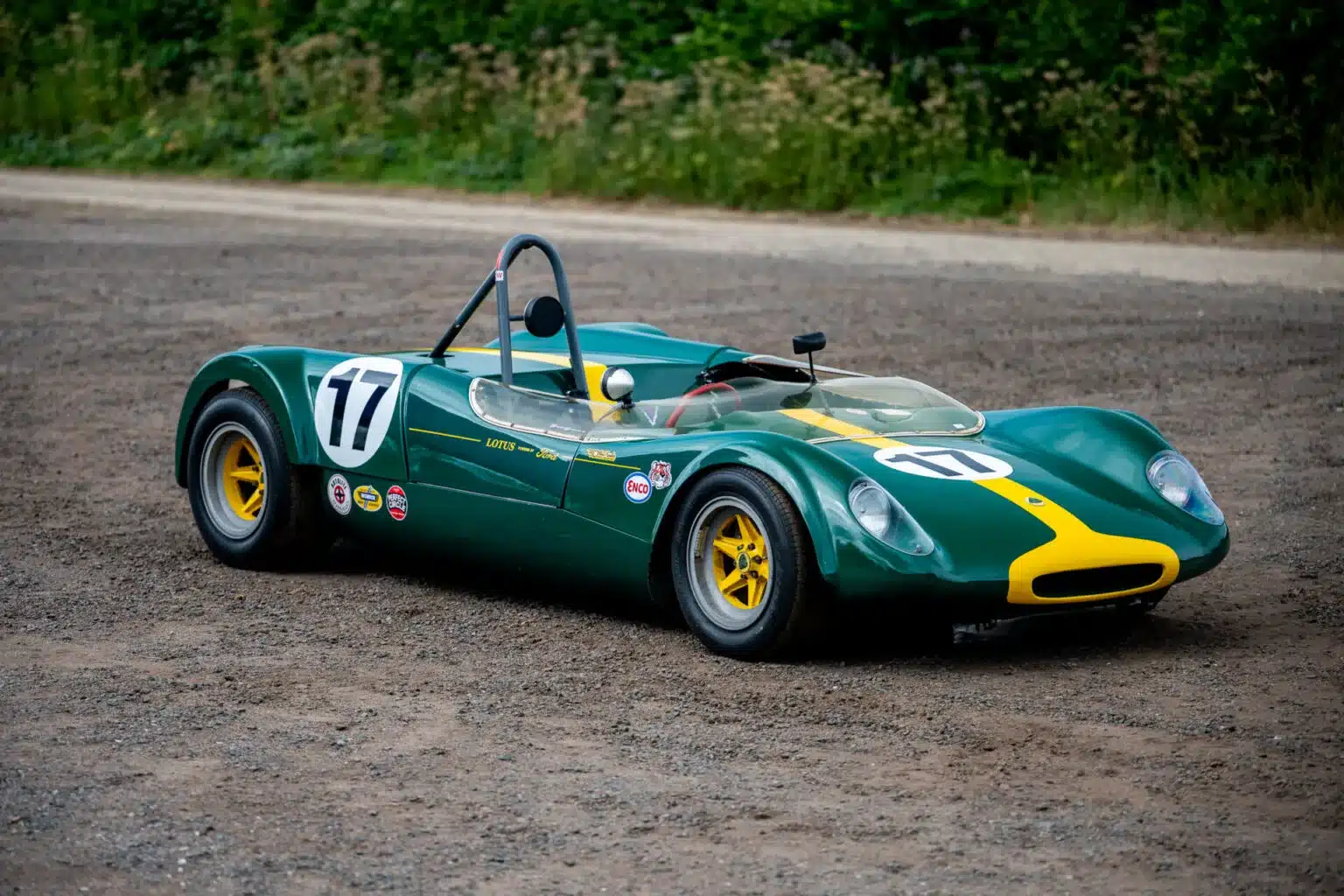 Historischer Lotus 23C Rennwagen, British Racing Green mit gelbem Streifen, auf Schotterplatz.