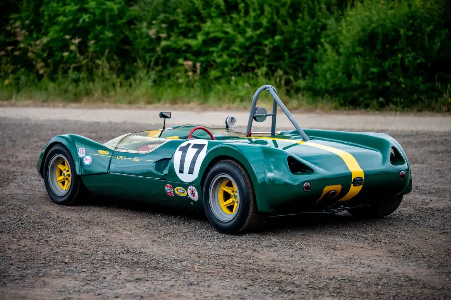 Lotus 23C Rennwagen in klassischem British Racing Green mit gelben Akzenten, fotografiert von hinten auf Schotter vor Grün.