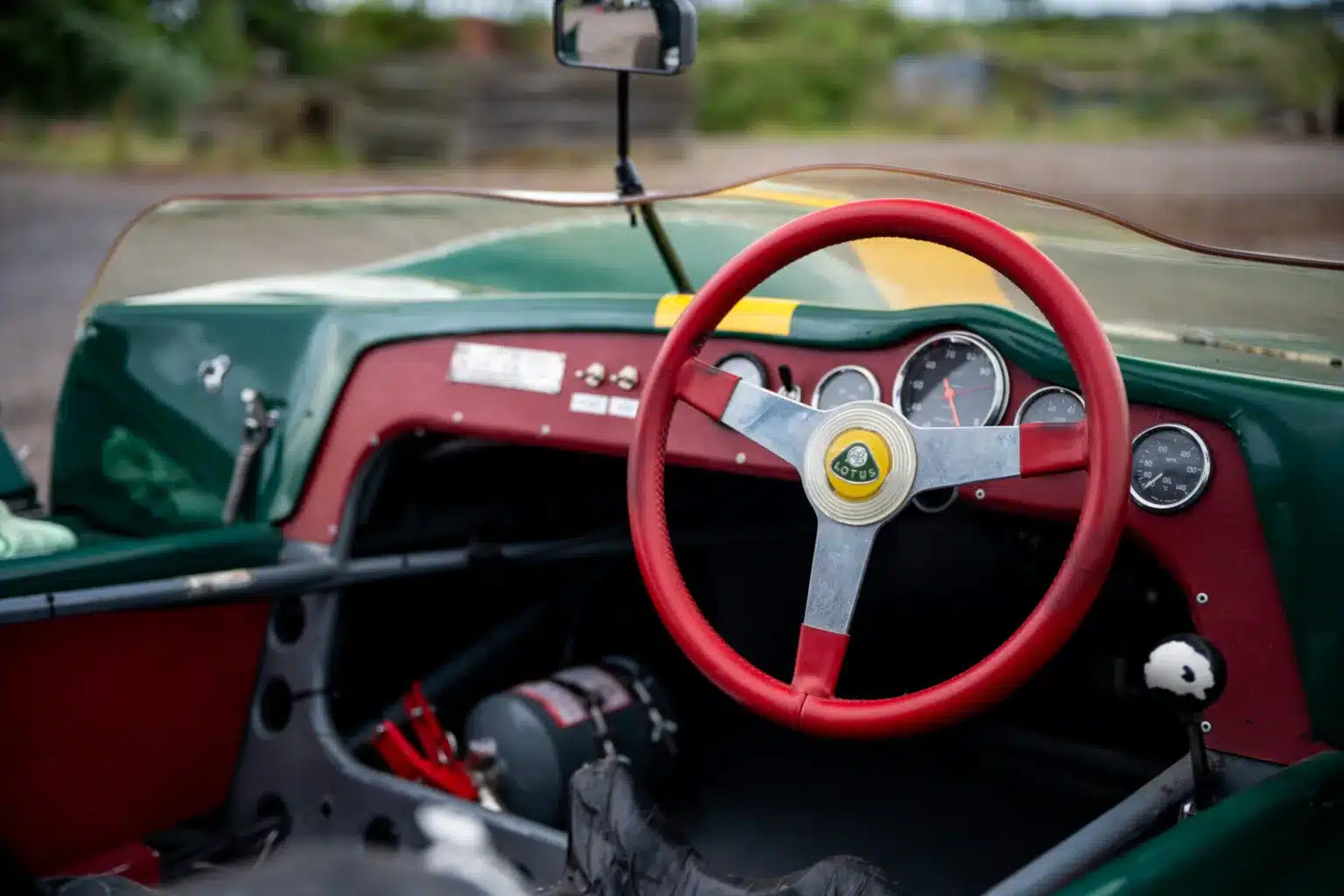 Innenraum eines historischen Lotus 23C Rennwagens mit rotem Lenkrad, klassischen Rundinstrumenten und grün-gelbem Karosserieausschnitt