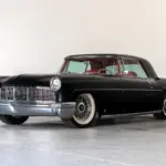 Schwarzer Continental Mark II von 1956, modernisiert als Resto-Mod, mit rotem Interieur und Drahtspeichenrädern, seitlich fotografiert vor hellem Hintergrund.