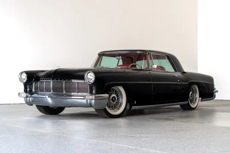 Schwarzer Continental Mark II von 1956, modernisiert als Resto-Mod, mit rotem Interieur und Drahtspeichenrädern, seitlich fotografiert vor hellem Hintergrund.
