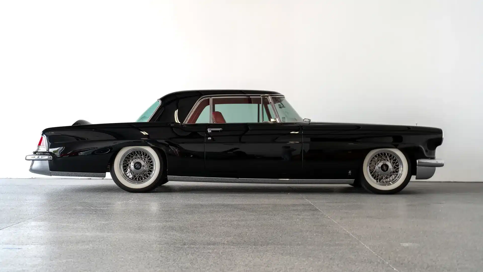 Restaurierter Continental Mark II von 1956 in Schwarz, Tieferlegung und Weißwandreifen, Seitenansicht vor weißer Wand.