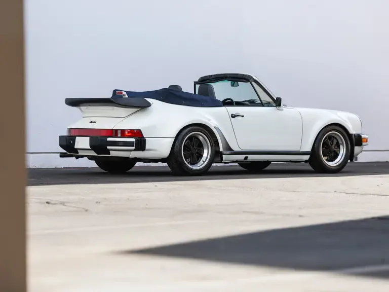 Weißes Porsche 911 Turbo Cabriolet, Baujahr 1989, Seiten- und Heckansicht mit geöffnetem Verdeck und markanter Turbo-Heckpartie.