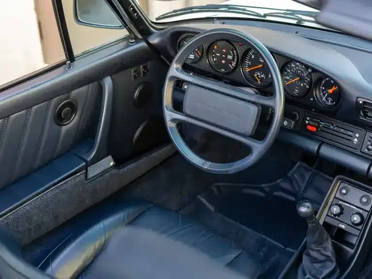 Innenraumansicht eines Porsche 911 Turbo Cabriolet von 1989 mit marineblauen Ledersitzen, klassischem Porsche-Dashboard und G50-Schaltgetriebe.