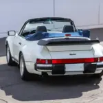 Heckansicht eines weißen Porsche 911 Turbo Cabriolet (Baureihe 930) Baujahr 1989 mit offenem Verdeck und markantem Heckspoiler.