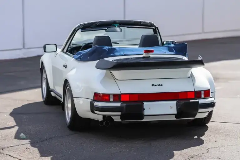 Heckansicht eines weißen Porsche 911 Turbo Cabriolet (Baureihe 930) Baujahr 1989 mit offenem Verdeck und markantem Heckspoiler.