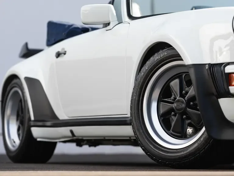 Detailaufnahme des hinteren Bereichs eines weißen Porsche 911 Turbo Cabriolets (Baureihe 930) mit markanter Karosserie und klassischer Felge.