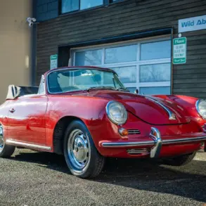 Rubyrotes Porsche 356C Cabriolet von 1965 mit geöffnetem Verdeck, seitlich und frontal fotografiert vor einer Garage.
