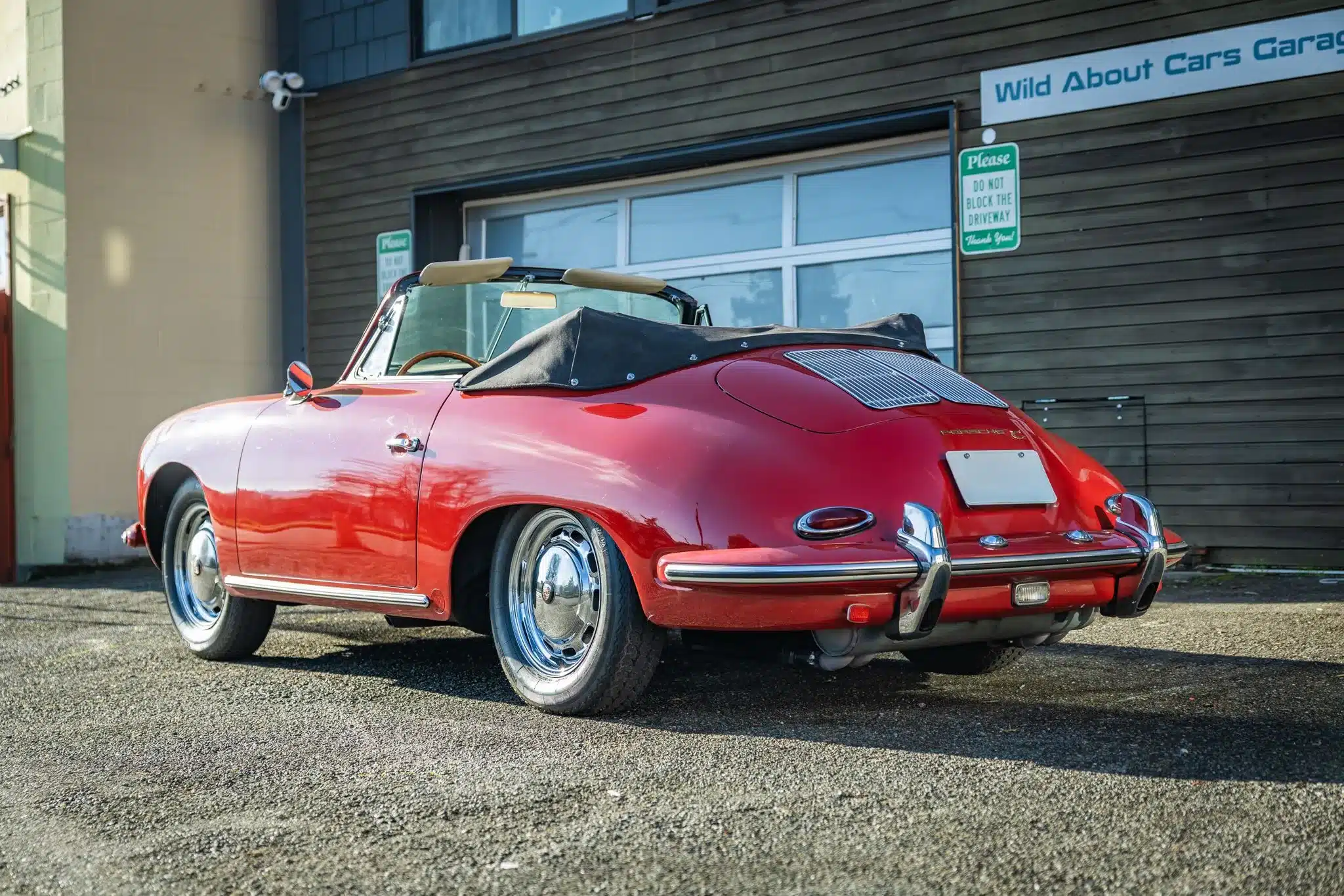 Porsche 356C Cabriolet von 1965 in rubinroter Lackierung mit schwarzem Stoffverdeck, Heckansicht vor einer Garage.