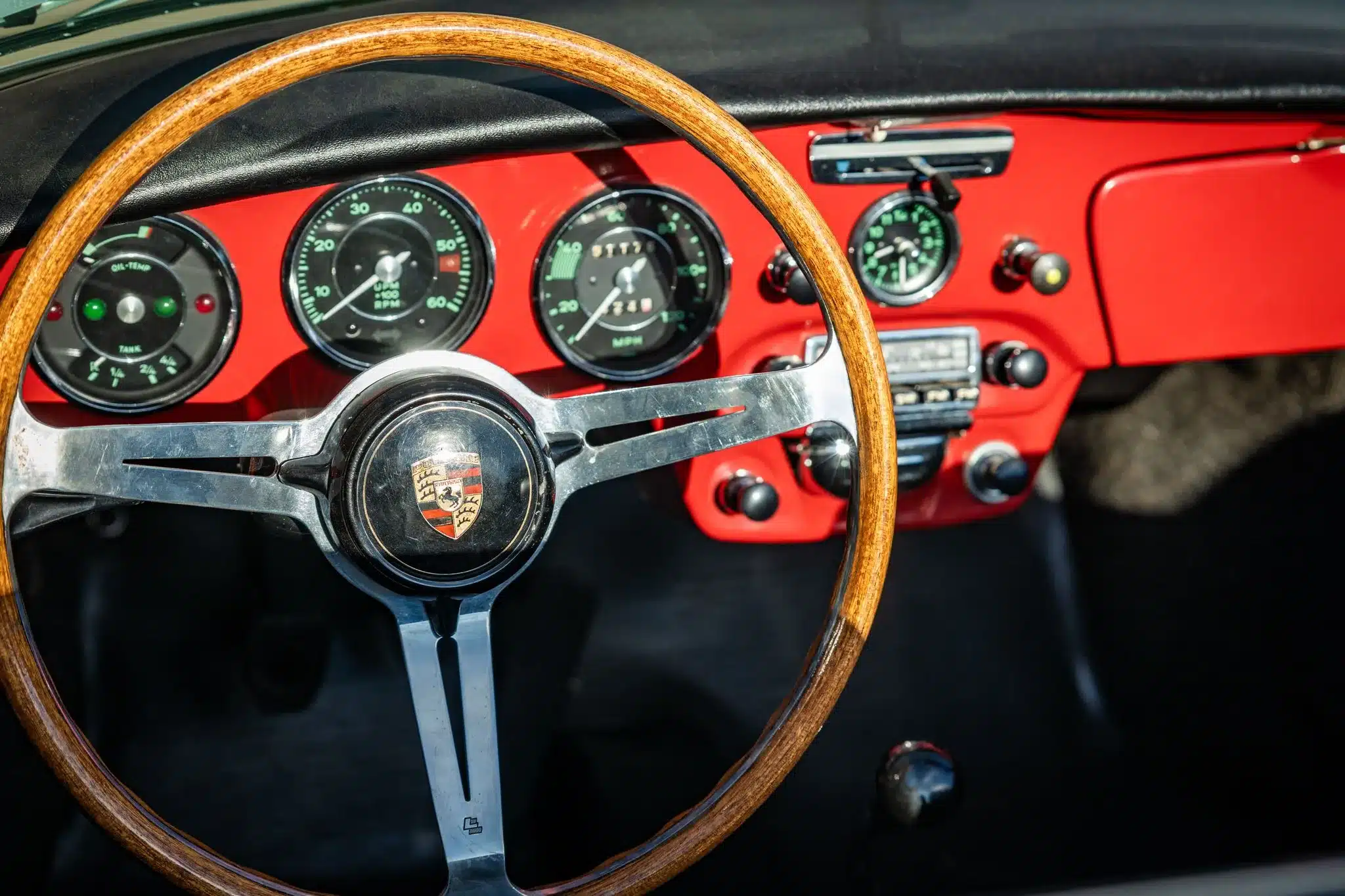 Innenraum eines Porsche 356C Cabriolet von 1965 mit Holzlenkrad, klassischen Instrumenten und rotem Armaturenbrett.