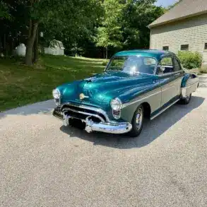 Grüner Oldsmobile 88 aus dem Jahr 1950 auf einer Einfahrt vor einem Wohnhaus, seitliche Frontansicht.