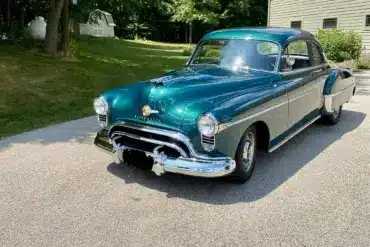 Grüner Oldsmobile 88 aus dem Jahr 1950 auf einer Einfahrt vor einem Wohnhaus, seitliche Frontansicht.