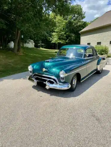 Grüner Oldsmobile 88 aus dem Jahr 1950 auf einer Einfahrt vor einem Wohnhaus, seitliche Frontansicht.