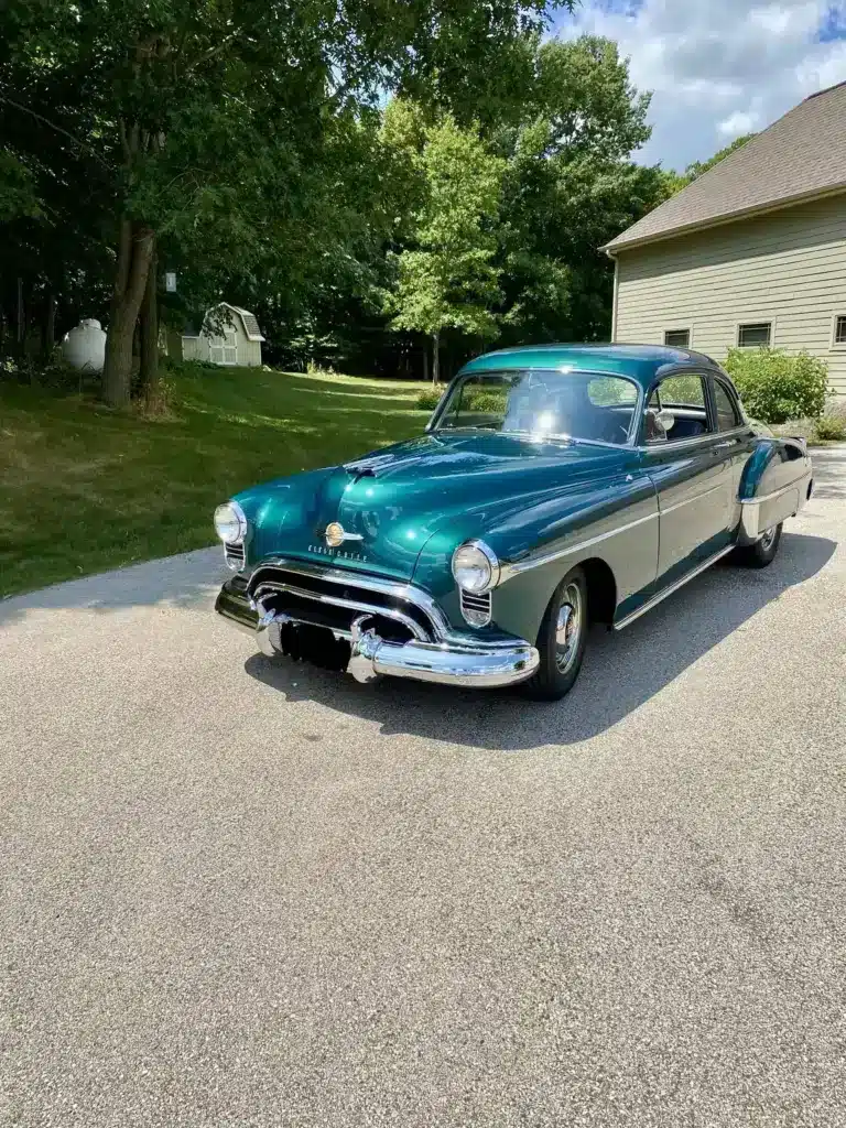 Grüner Oldsmobile 88 aus dem Jahr 1950 auf einer Einfahrt vor einem Wohnhaus, seitliche Frontansicht.