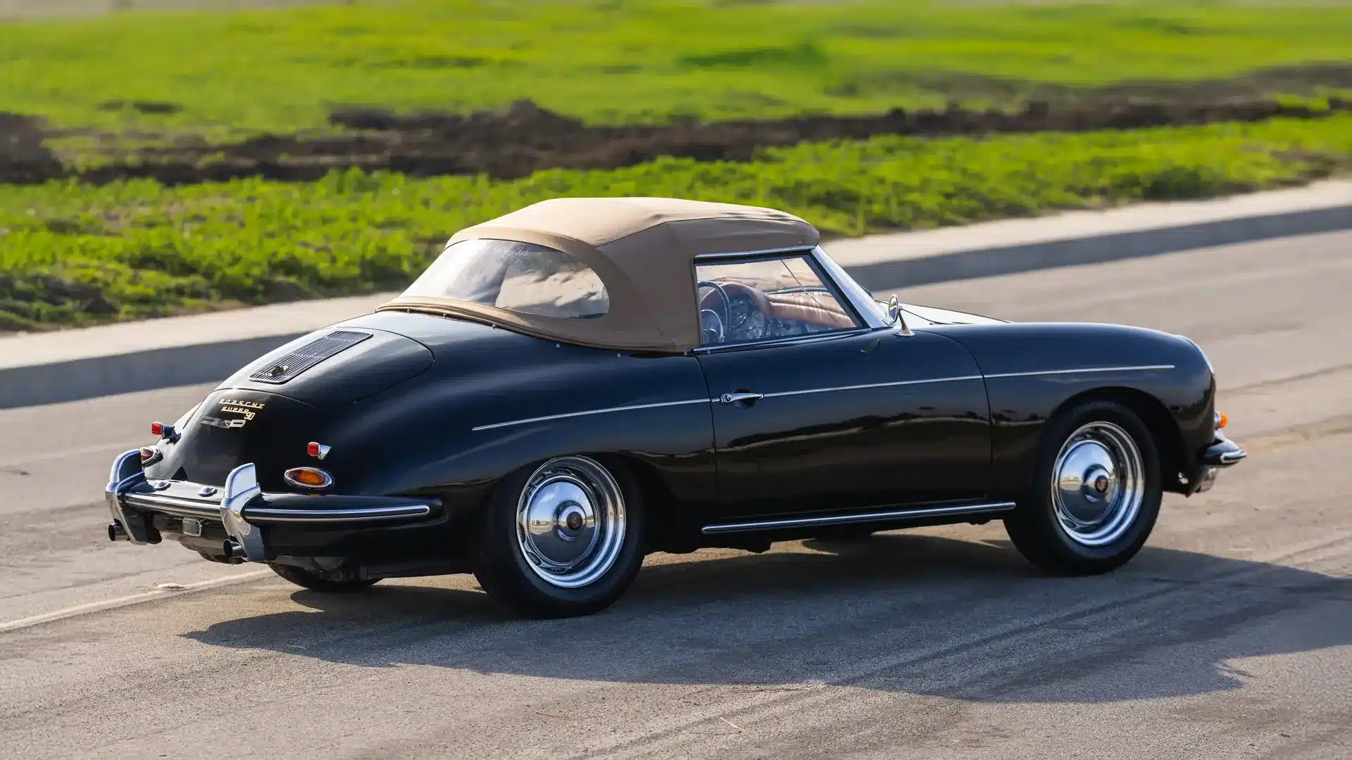 Porsche 356 B Super 90 Roadster von 1960 in Schwarz mit beigem Stoffverdeck, aufgenommen auf einer Straße vor grüner Landschaft